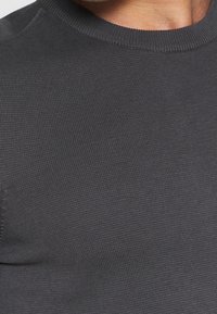Dunkelgrauer Strickpullover mit geripptem Rundhalsausschnitt und glatter Textur, mit einer Nahaufnahme des Stoffes.