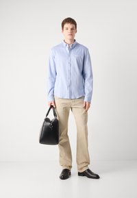 Lichtblauw overhemd met kraag, beige broek, zwarte leren schoenen en een zwarte leren handtas met dubbele rits en een gebogen bovenkant.