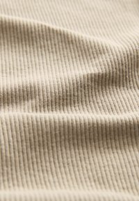 Tessuto beige a coste con sottili linee verticali, caratterizzato da una morbida texture e delicate variazioni di tonalità sulla superficie.