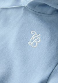 Jasnoniebieska bluza z miękką fakturą i białym haftowanym logo na piersi. Model z kapturem o luźnym kroju.