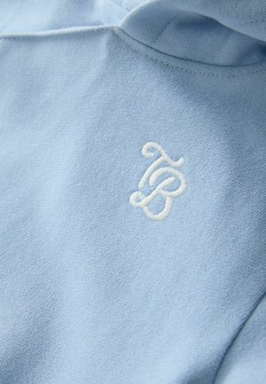 Gaiši zilas krāsas džemperis ar mīkstu audumu un baltu izšūtu logotipu uz krūtīm. Dizains ar kapuci un brīvu piegriezumu.