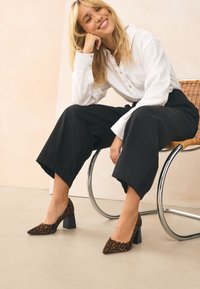 Décolleté con stampa leopardata, punta a punta e tacco alto spesso nero; abbinate a pantaloni neri larghi e una camicia bianca con bottoni.