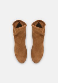 Beżowe zamszowe botki sięgające kostki o miękkiej strukturze i złożonym projekcie górnej części, z gładkim wykończeniem i smukłą sylwetką.