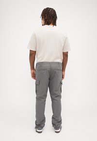Khaki cargobroek met zijzakken, grijze kleur, relaxte pasvorm. Lichtbeige t-shirt. Zachte stoftextuur, eenvoudig ontwerp en rechte pijp.