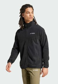 Black fleece jacket with a high collar, zip front, and subtle Terrex logo; features a smooth texture and two side pockets.