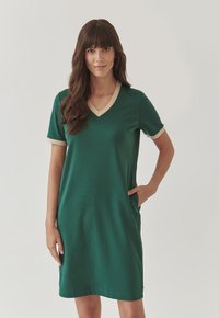 Green short-sleeve dress with a V-neckline and beige accents at the collar and sleeves. Features side pockets and a relaxed fit.