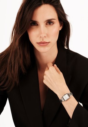 Sølv rektangulært ur med en hvid skive og sorte accenter, båret på et håndled, med et poleret metalarmbånd og et minimalistisk design.