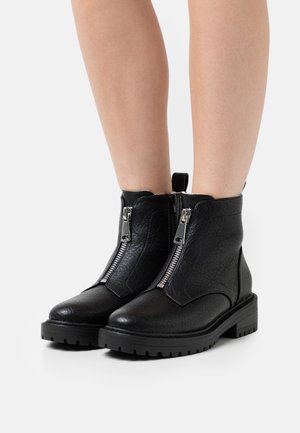 Bottines en cuir noir avec une finition texturée, dotées de fermetures éclair latérales doubles et d'une semelle à crampons épaisse. Le design comprend une bride de traction à l'arrière.