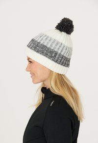 Stickad vintermössa i krämfärgad och grå med en pom-pom på toppen. Har växelvis randning och ribbad textur för extra värme.