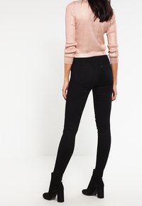 Jeans negros ajustados de cintura alta con bolsillos traseros, combinados con un suéter de punto ribeteado en rosa claro y botas de tacón negras.