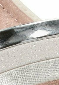 Detallado de correa metálica plateada sobre una parte superior sintética de color rosa pálido, con acentos texturizados y brillantes, vista en primer plano.