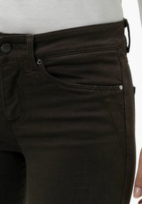 Vaqueros de mezclilla marrones con corte slim, que cuentan con un cierre de botón y cremallera, bolsillos frontales y detalles de costura en contraste.