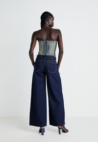 Denim korzet s zipem, v kombinaci s širokými tmavě modrými džíny. Tmavě fialové sandály na podpatku dokončují vzhled.