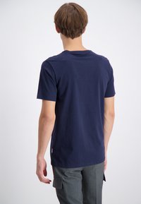 Tummansininen puuvillapaita, jossa on miehustakaulus, lyhyet hihat ja kapea leikkaus. Materiaalin pinta näyttää pehmeältä ja sileältä.