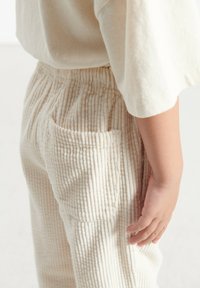 Pantalons en velours côtelé beige clair à rayures verticales, avec taille élastique et poche latérale. Assortis à une chemise décontractée de couleur claire.