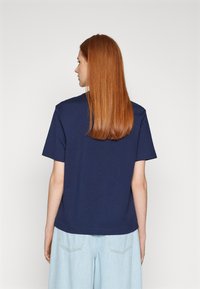 Navy blue cotton t-shirt with short sleeves, a round neckline, and a relaxed fit, viewed from the back. Light wash denim shorts.