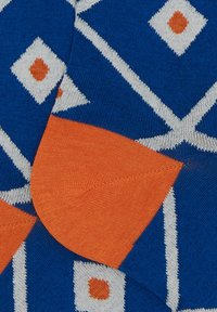 Calzini lavorati a maglia con uno sfondo blu e un motivo geometrico a rombi in bianco, dettagli arancioni e una sezione del tallone a trama arancione.