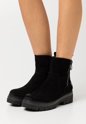 Botas negras de ante hasta el tobillo con un acabado texturizado, cremallera lateral y suelas gruesas de goma con un patrón de banda de rodadura resistente.