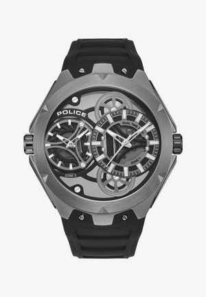 Orologio con cinturino in gomma nera che mostra due fusi orari, con cassa in metallo argentato e nera, design scheletrato e finiture raffinate sui quadranti.