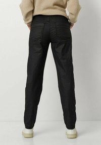 Schwarze, maßgeschneiderte Hose im geraden Schnitt, mit zwei Gesäßtaschen und einer glatten Textur. Kombiniert mit cremefarbenen Sneakers.