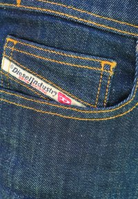 Tissu en denim bleu marine avec une texture visible, présentant des coutures orange et une petite étiquette blanche portant l'inscription "Diesel Industry Denim Division".