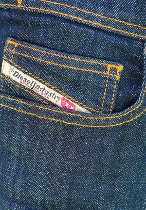 Tessuto di denim blu scuro con trama visibile, caratterizzato da cuciture arancioni e una piccola etichetta bianca con la scritta "Diesel Industry Denim Division".