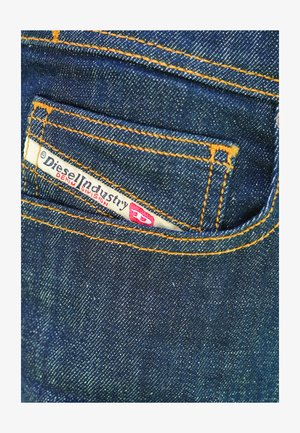 Tessuto di denim blu scuro con trama visibile, caratterizzato da cuciture arancioni e una piccola etichetta bianca con la scritta "Diesel Industry Denim Division".