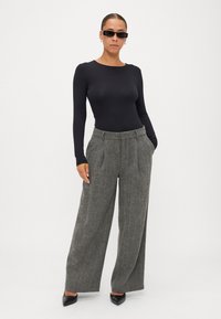 Melna krekla ar garām piedurknēm, pelēki houndstooth plaša stila bikses ar priekšējiem krokām, un melni norādīti zābaki. Minimalistiskas melnas saulesbrilles papildina izskatu.