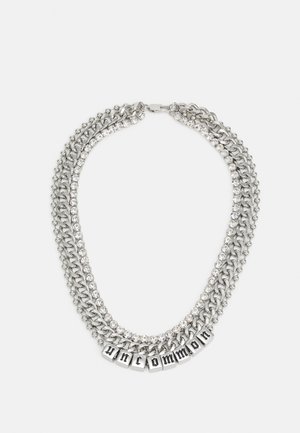 Colar prateado de várias camadas com correntes metálicas e detalhes em strass, apresentando blocos com letras que formam a palavra "uncommon" ao centro.