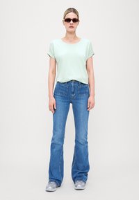 Lys myntegrønn kortermet topp med rullekanter, kombinert med blå jeans med vide ben og frontlommer. Solbriller gir et elegant preg.