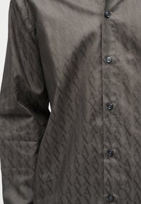 Σκούρο γκρι πουκάμισο με κουμπιά, με ένα διακριτικό επαναλαμβανόμενο γεωμετρικό σχέδιο και μακριά μανίκια.