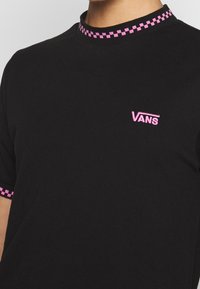 T-shirt noir avec motif à carreaux roses au col et aux manches. Présente un petit logo Vans rose brodé sur la poitrine.