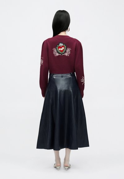 Borvörös kötött pulóver virágos hímzéssel a háton, fekete bőr midi szoknyával, amely lágyan bővül.