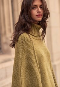 Olive green knitted sweater with a high ribbed collar, featuring a loose fit and textured pattern, highlighting warm and cozy material.