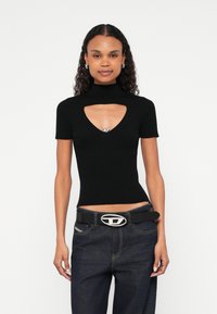 Μαύρο τοπ με ριμπ υφή, κοντά μανίκια και V-λαιμόκοψη με άνοιγμα, διακοσμημένο με ασημί λεπτομέρεια. Συνδυασμένο με ψηλόμεσο σκούρο τζιν και μαύρη ζώνη.