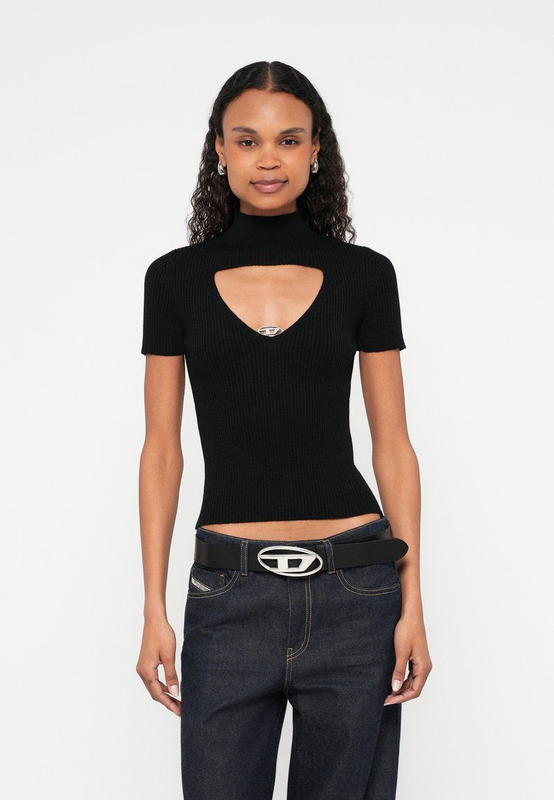 Μαύρο τοπ με ριμπ υφή, κοντά μανίκια και V-λαιμόκοψη με άνοιγμα, διακοσμημένο με ασημί λεπτομέρεια. Συνδυασμένο με ψηλόμεσο σκούρο τζιν και μαύρη ζώνη.