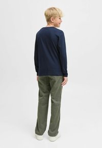 Camicia a maniche lunghe blu navy abbinata a pantaloni casual verde oliva. La camicia ha un collo rotondo, mentre i pantaloni presentano una vestibilità comoda e cuciture a vista.