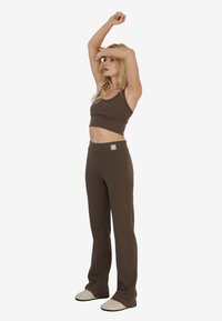Brązowy prążkowany crop top i dopasowane spodnie z wysokim stanem. Top ma cienkie ramiączka. Strój posiada mały detal akcentujący na pasku.