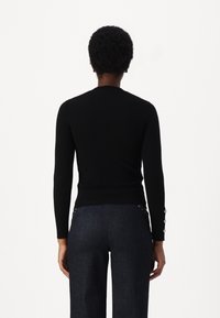 Haut noir à manches longues côtelées avec une coupe ajustée. Présente un col rond et des détails de boutons aux poignets. Texture lisse.