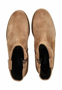 Braune Wildleder-Stiefeletten mit runder Zehenpartie und seitlichem Reißverschluss. Enthält ein kleines Band-Detail an der Seite. Weiche Textur und minimalistisches Design.