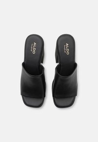 Svarte lærsklie-sandaler med bredt frontreim og åpen tå. Blokkhæl og merket såle-design gir funksjonelle detaljer.