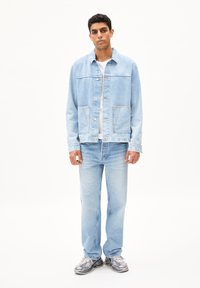 Lichtblauw denim jack met een ontspannen pasvorm, twee voorkruiden en een recht gesneden stijl. Gecombineerd met lichtblauwe jeans en grijze sneakers.