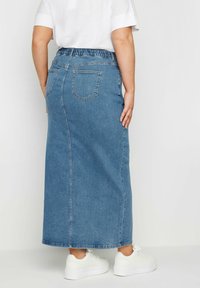 Denim-maksihame, jossa on joustava vyötärö, sininen väri, kaksi takataskua ja suora siluetti, yhdistettynä valkoisiin tennareihin.