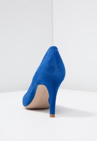 Modrá semišová vysoce podpatková bota s špičatou špičkou, štíhlým stiletto podpatkem a hladkým povrchem. Interiér ukazuje béžovou stélku s označením značky.