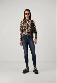 Duga leopard print bluza sa dugim rukavima u kombinaciji s visokim tamnim trapericama i čizmama s debelim potplatima, s podesivim trakama i elegantnom torbicom.