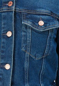 Dark blue denim jacket featuring copper buttons, a chest pocket, and contrasting stitching, highlighting a classic design and texture.