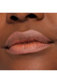 Nærbilde av lepper med en matte nude leppestiftfarge, glatt tekstur og godt definert form mot en rik brun hudtone.