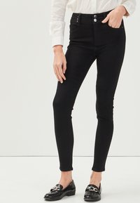Jeans neri a vita alta con una vestibilità slim, dotati di due tasche anteriori e due bottoni in vita. Tessuto liscio e senza fantasie.