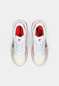 Λευκά αθλητικά παπούτσια τρεξίματος με κόκκινες λεπτομέρειες, μαλακή περιφέρεια και εξέχοντα μαύρο λογότυπο. Διαθέτουν υφή στο σχέδιο και ελαφρύ σχεδιασμό.