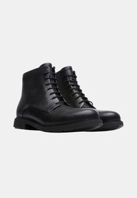 Bottines en cuir noir avec une texture lisse, bout rond et lacets traditionnels. Semelles en caoutchouc robustes au design minimaliste.